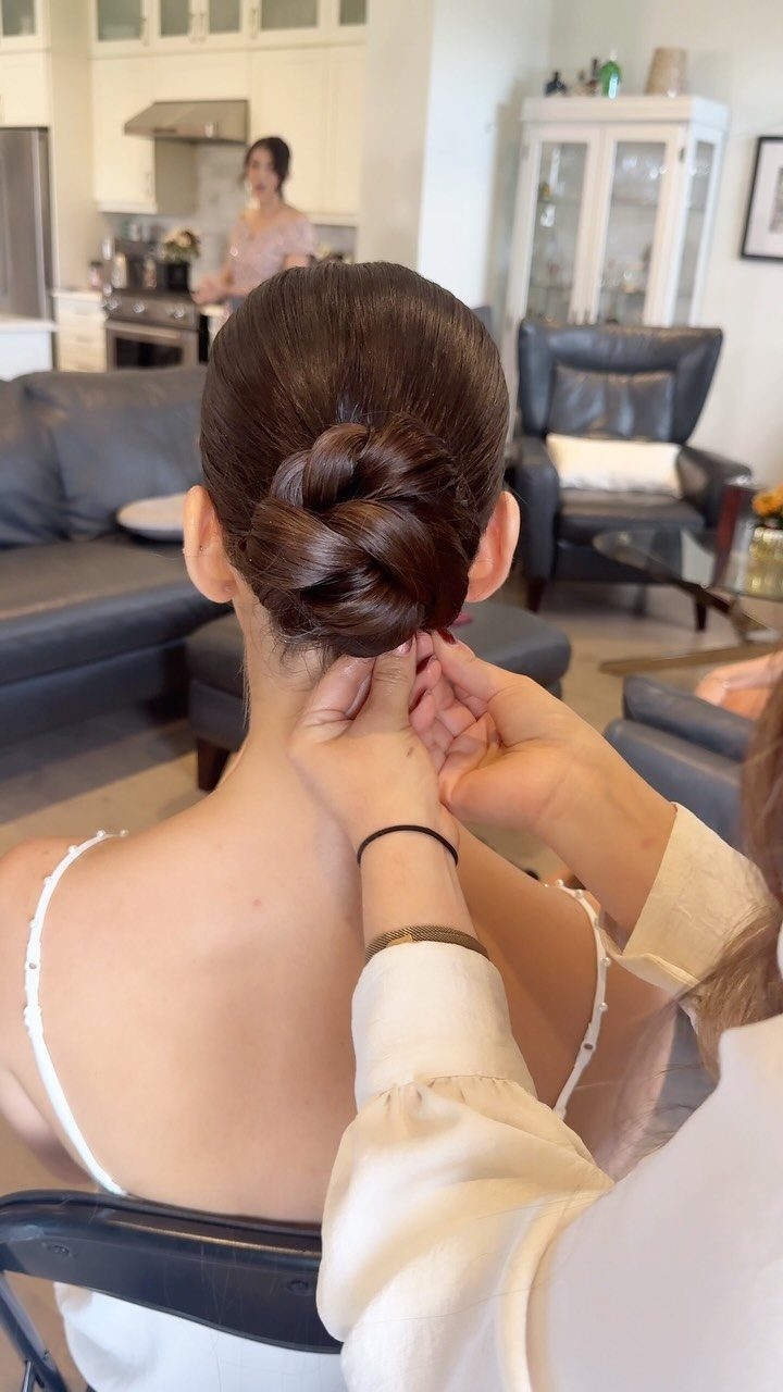 Woman with a polished low bun hairstyle being adjusted by another person's hands.