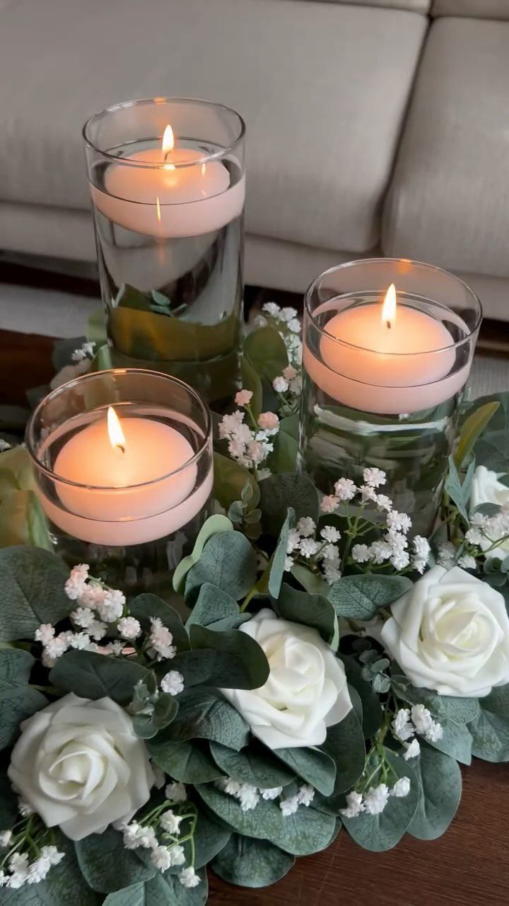 Floating white candles in glass cylinders surrounded by white roses and eucalyptus greenery