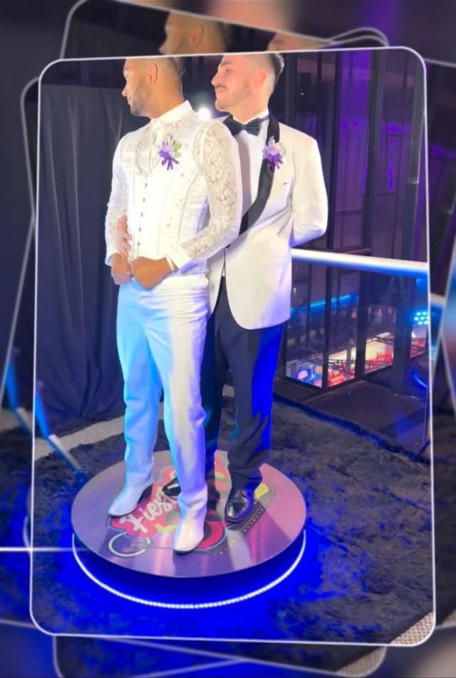 Two men in wedding suits standing on a circular 360 photo booth platform.