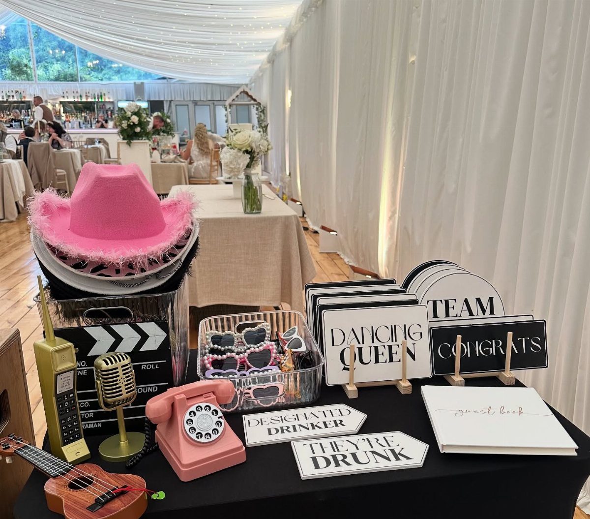 Wedding photo booth props including a pink cowboy hat, vintage phone, and speech bubbles.