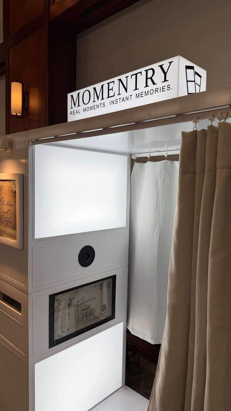 Enclosed white photo booth with tan privacy curtains and a Momentry brand sign.