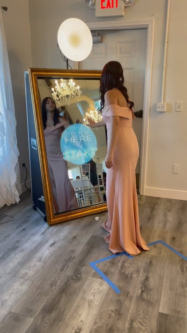 Woman in peach dress using a gold-framed magic mirror photo booth with digital prompts.