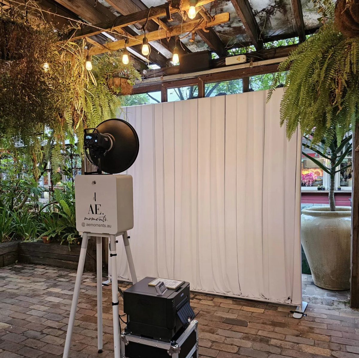 Open-air photo booth with white backdrop and professional lighting in a garden patio.