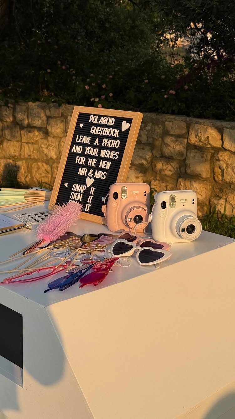 Two instant cameras and heart sunglasses on a table next to a guestbook sign.