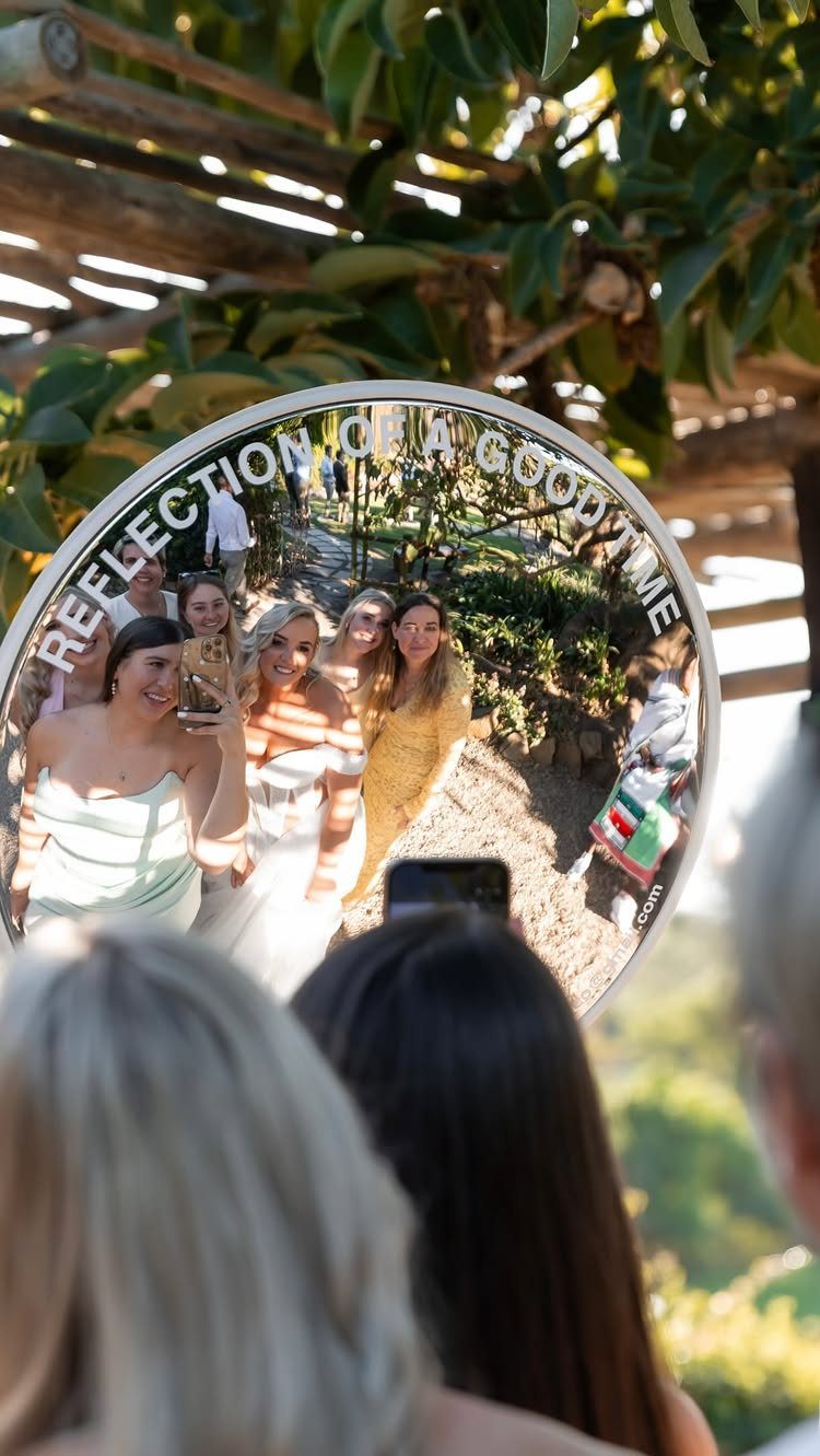 Women taking a group selfie in a large circular mirror at a wedding event