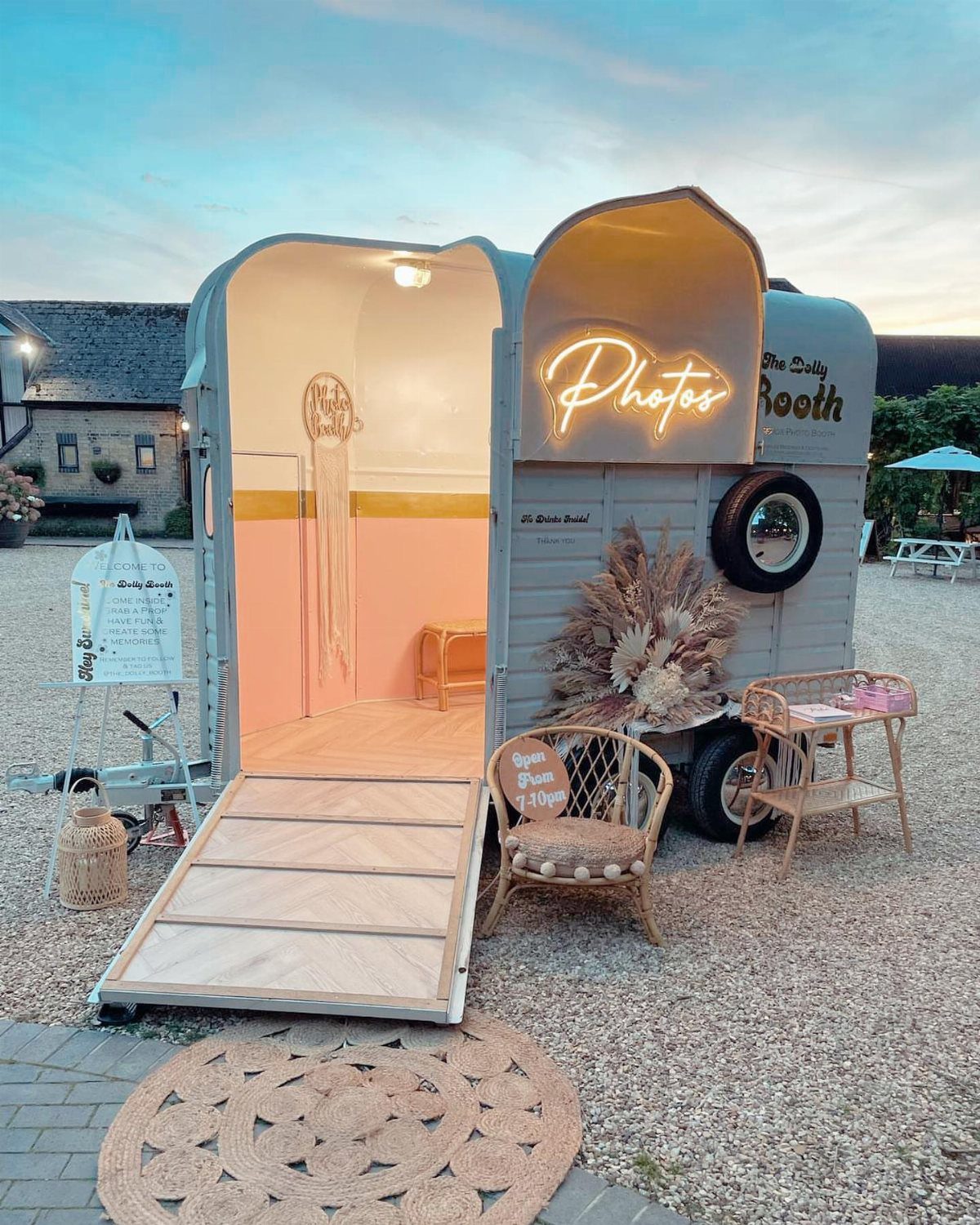 Vintage trailer photo booth with neon sign and wicker furniture on gravel ground