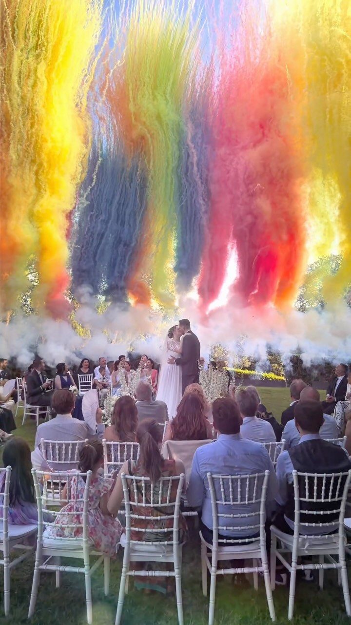 17 Wedding Ideas Pictures to Show Your Photographer 15 Wedding couple kissing before guests with colorful smoke bombs rising in the background.