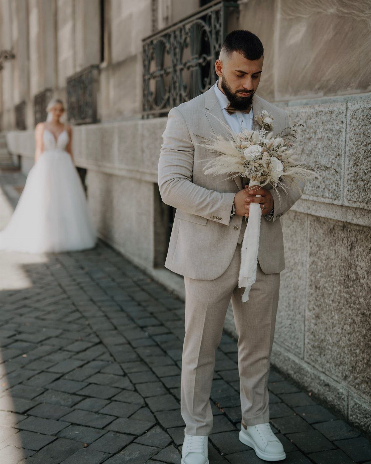 17 Wedding Ideas Pictures to Show Your Photographer 4 Groom in beige suit holding bouquet with bride blurred in background on cobblestone street