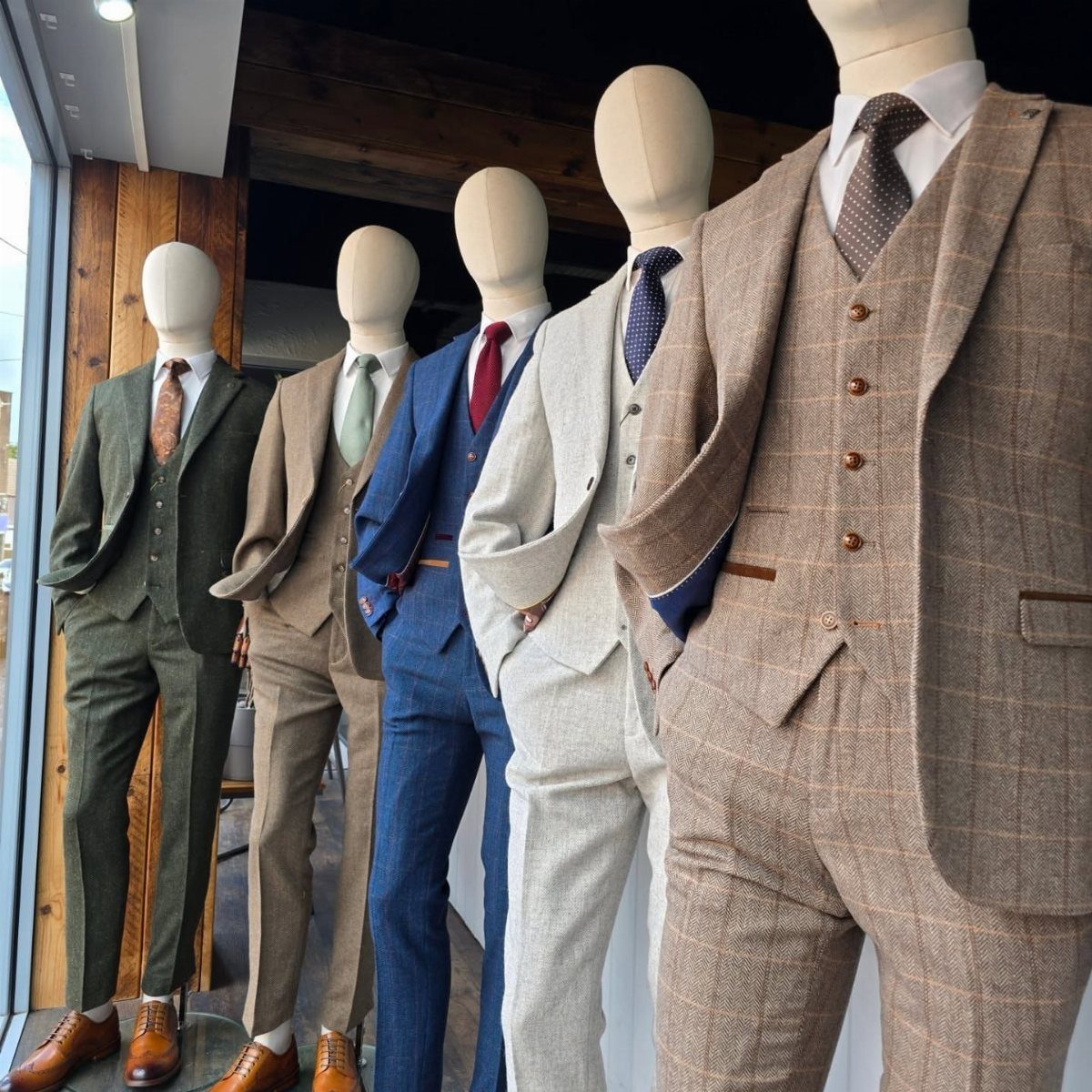Five mannequins wearing three-piece suits in olive, tan, navy, white, and brown plaid.