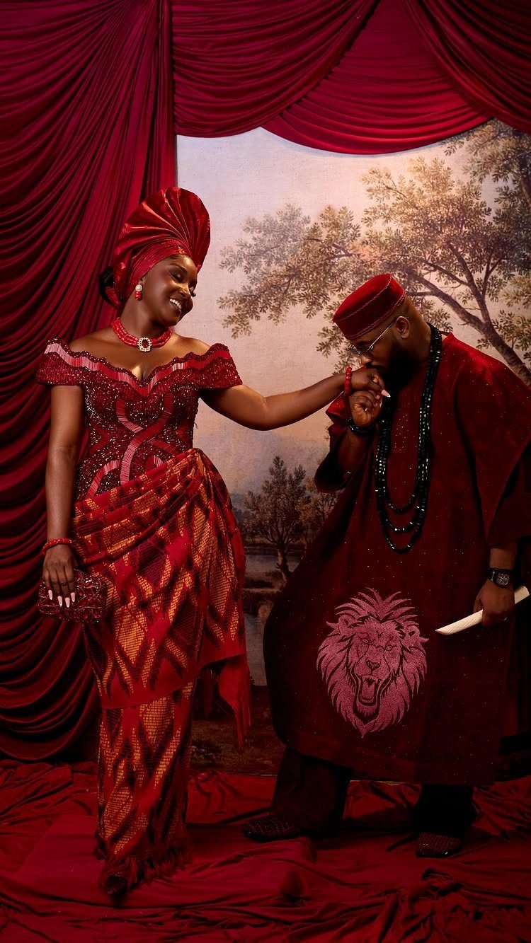 Couple in traditional red Nigerian wedding attire with a man kissing the woman's hand.