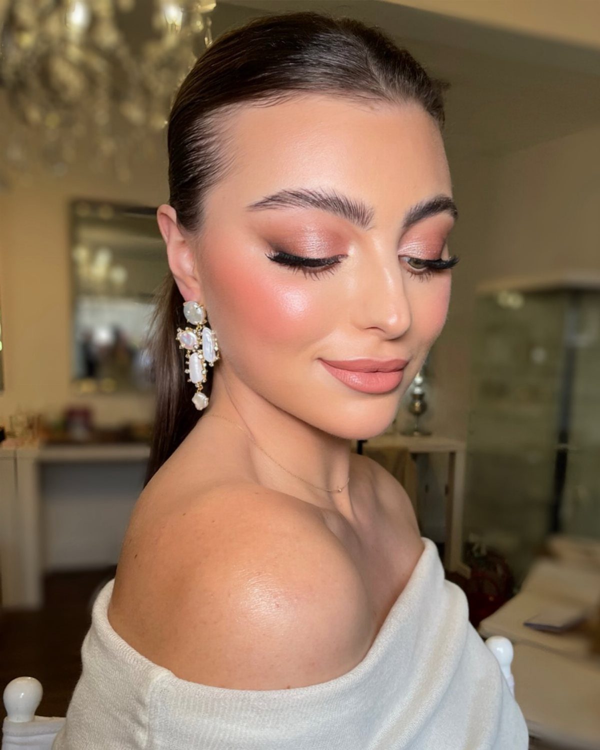 Woman with rosy blush and pink eyeshadow wearing a white off-the-shoulder top.