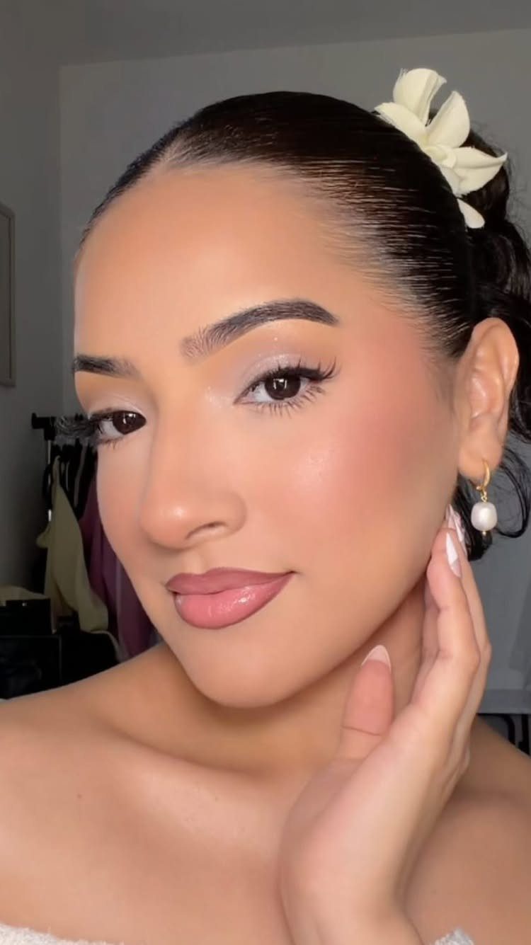 Woman with shimmering eye makeup, defined brows, and a white flower in her hair.