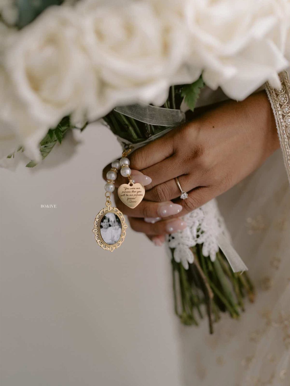 Hand holding white rose bouquet with a memorial photo charm and heart pendant.