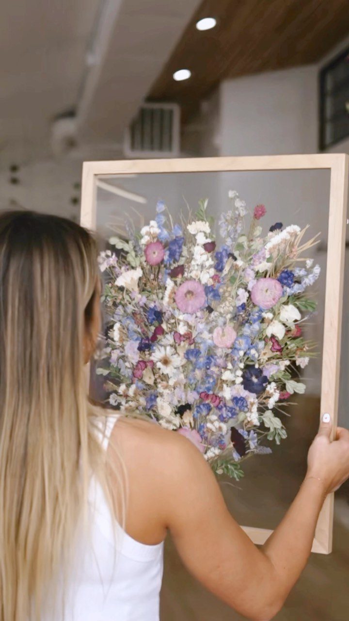 Pressed wedding bouquet of purple and pink flowers preserved in a wooden frame.