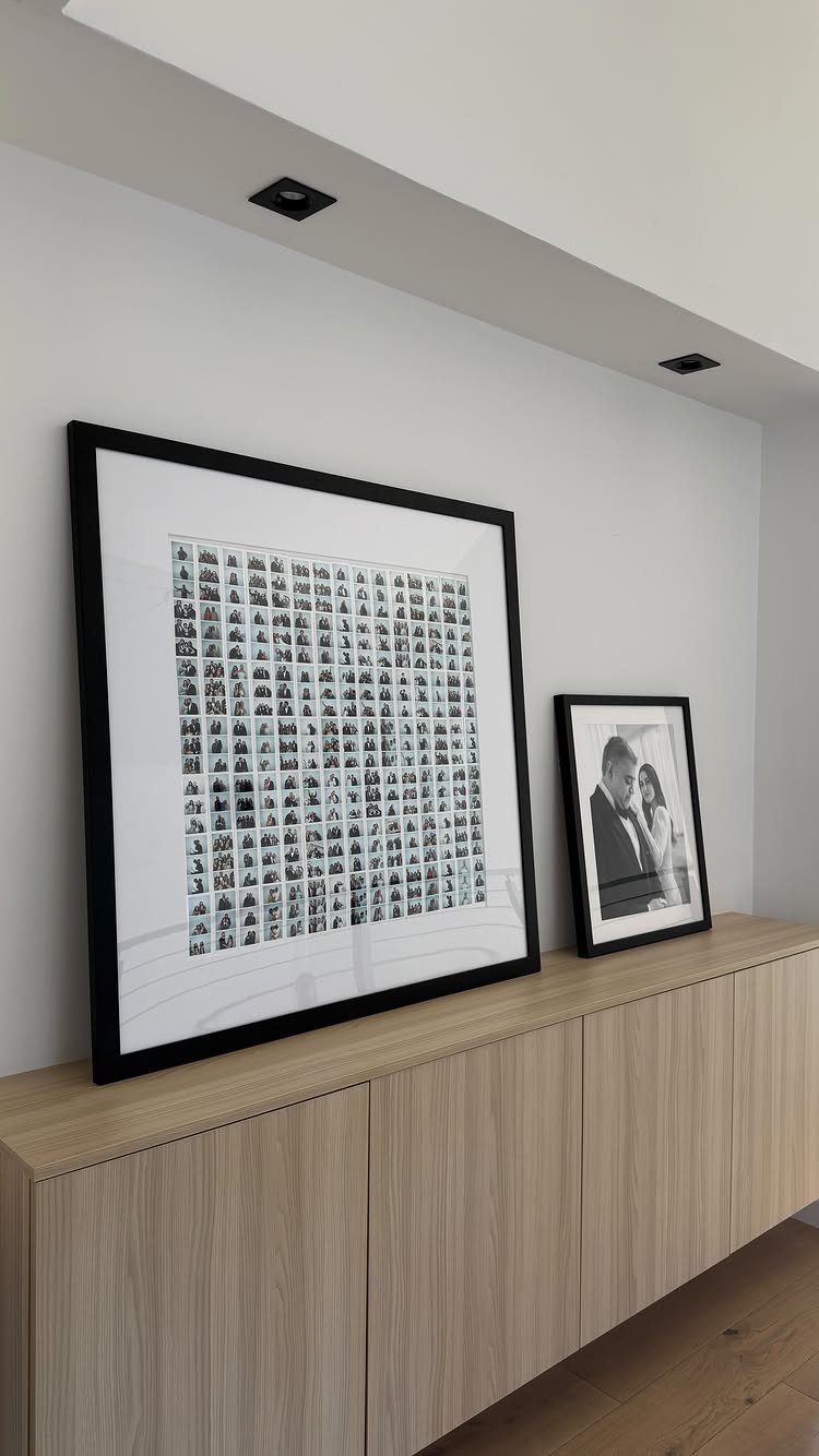 Framed wedding photo grid and couple portrait resting on a light wood cabinet.