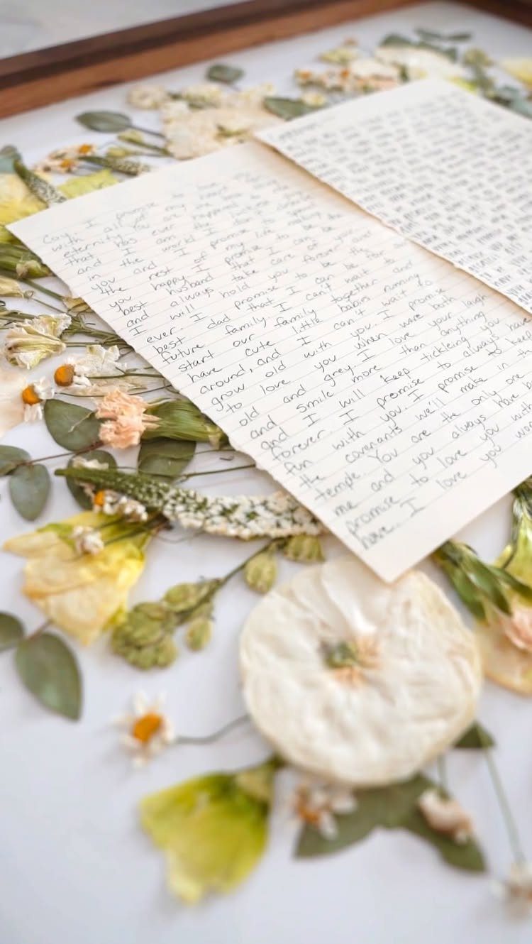 Handwritten letters and pressed dried flowers preserved inside a wooden shadow box frame.