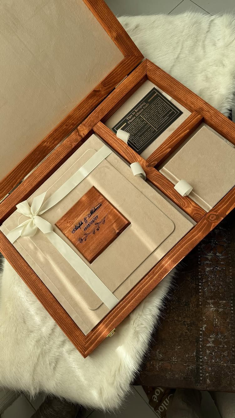 Beige fabric photo album with white ribbon inside a wooden keepsake box.