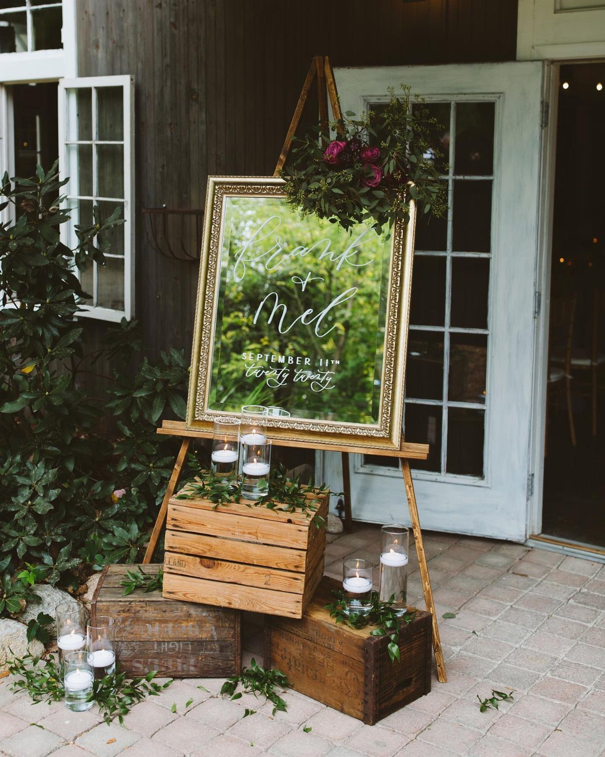Stacked wooden crates with candles and a framed mirror on an easel outdoors.