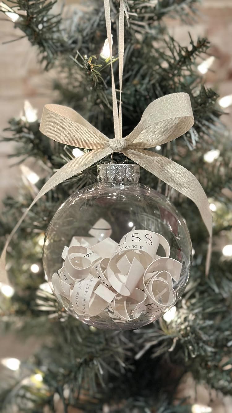 Clear glass ornament filled with white paper strips hanging on a lit evergreen tree