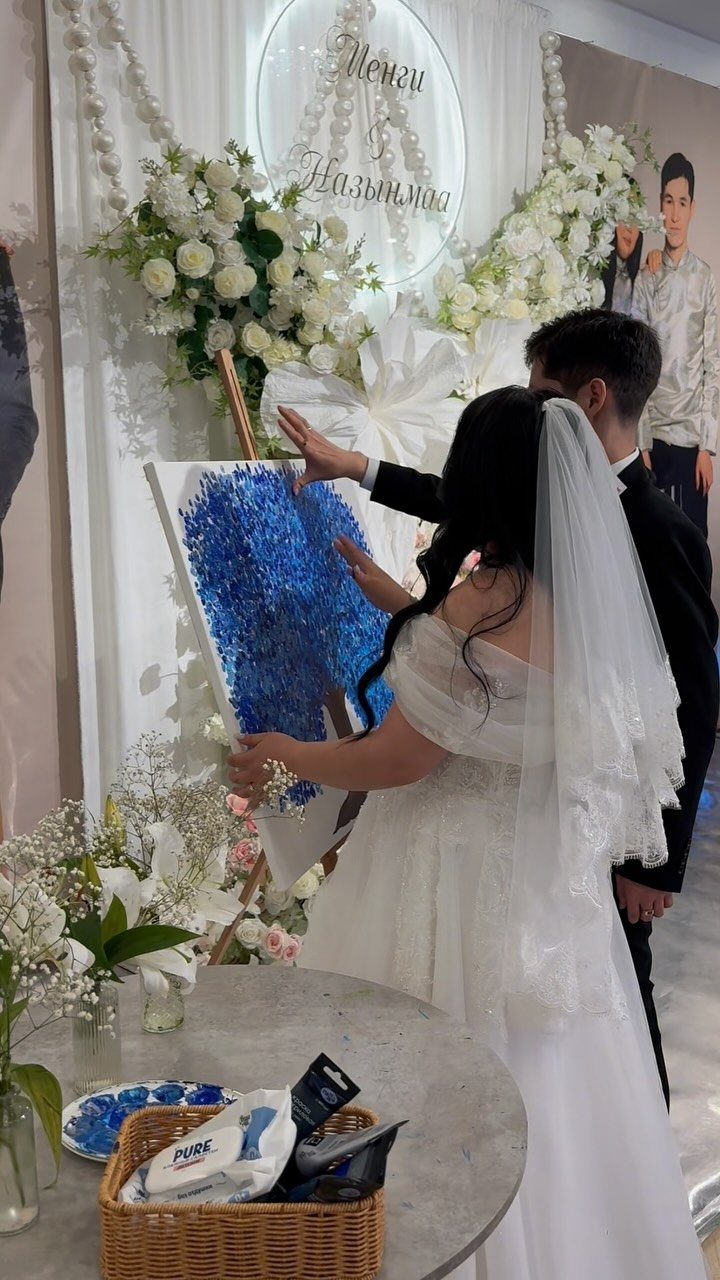 Bride and groom standing by a blue textured painting at a wedding reception.