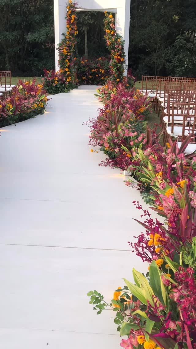 White wedding pergola covered in colorful flowers at the end of a floral aisle