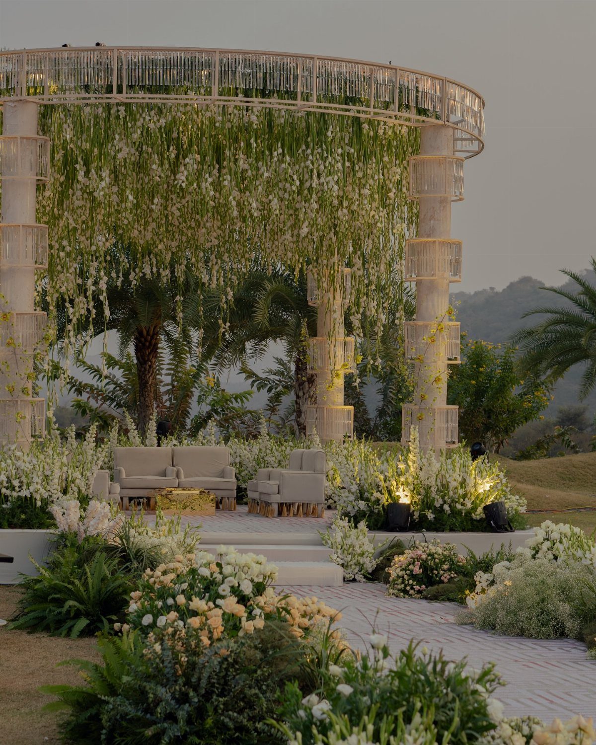 White circular pergola with hanging flowers and grey lounge seating in a garden