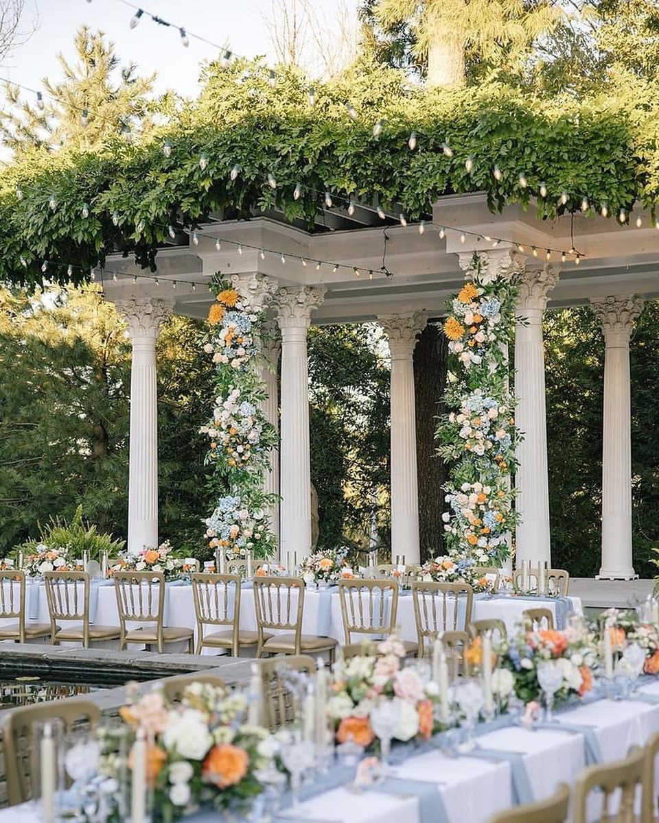 White classical pergola with climbing orange and white flowers and outdoor dining tables.