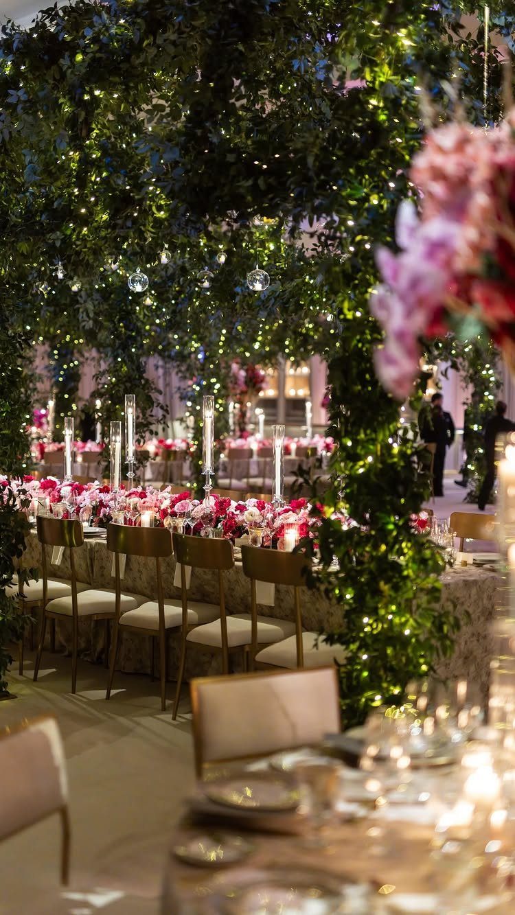 Wedding reception table under a lush green foliage canopy with twinkling fairy lights.