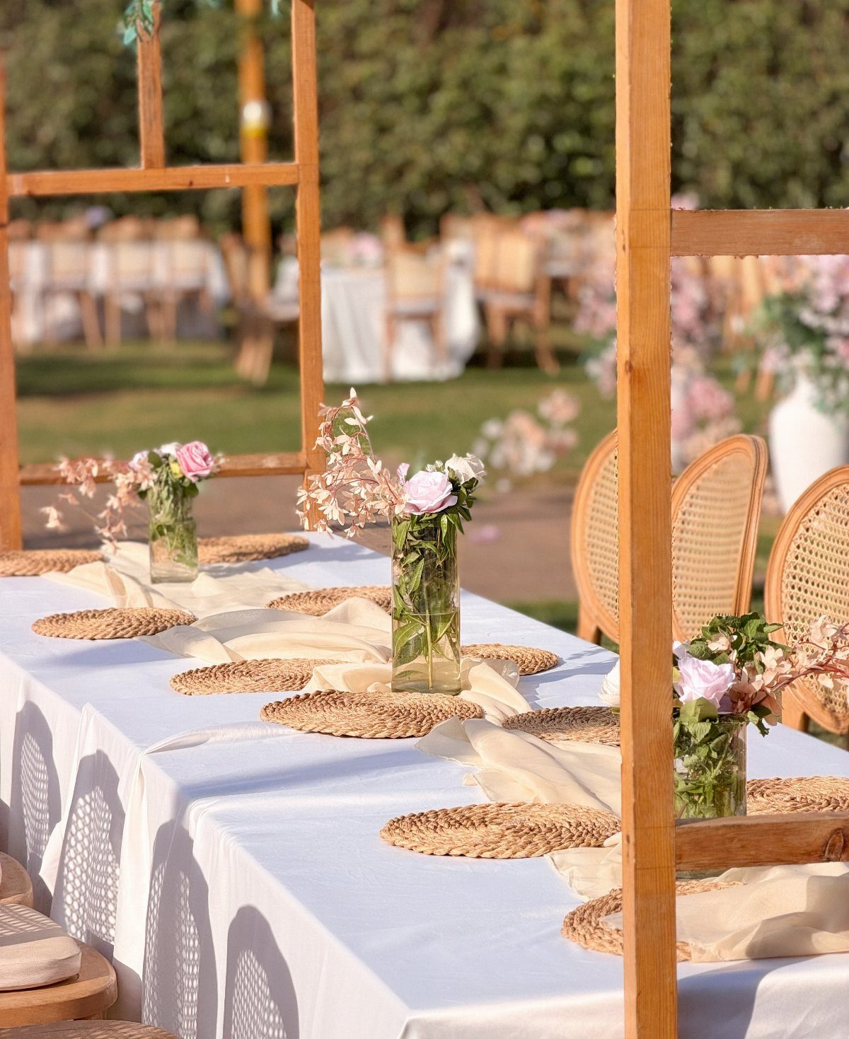 Wedding table with white linens and floral arrangements under a wooden pergola structure.