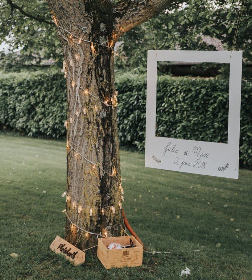 Best Wedding Photo Station Ideas: 8 Booths and Backdrops 7 White polaroid frame hanging from a tree with fairy lights in a garden