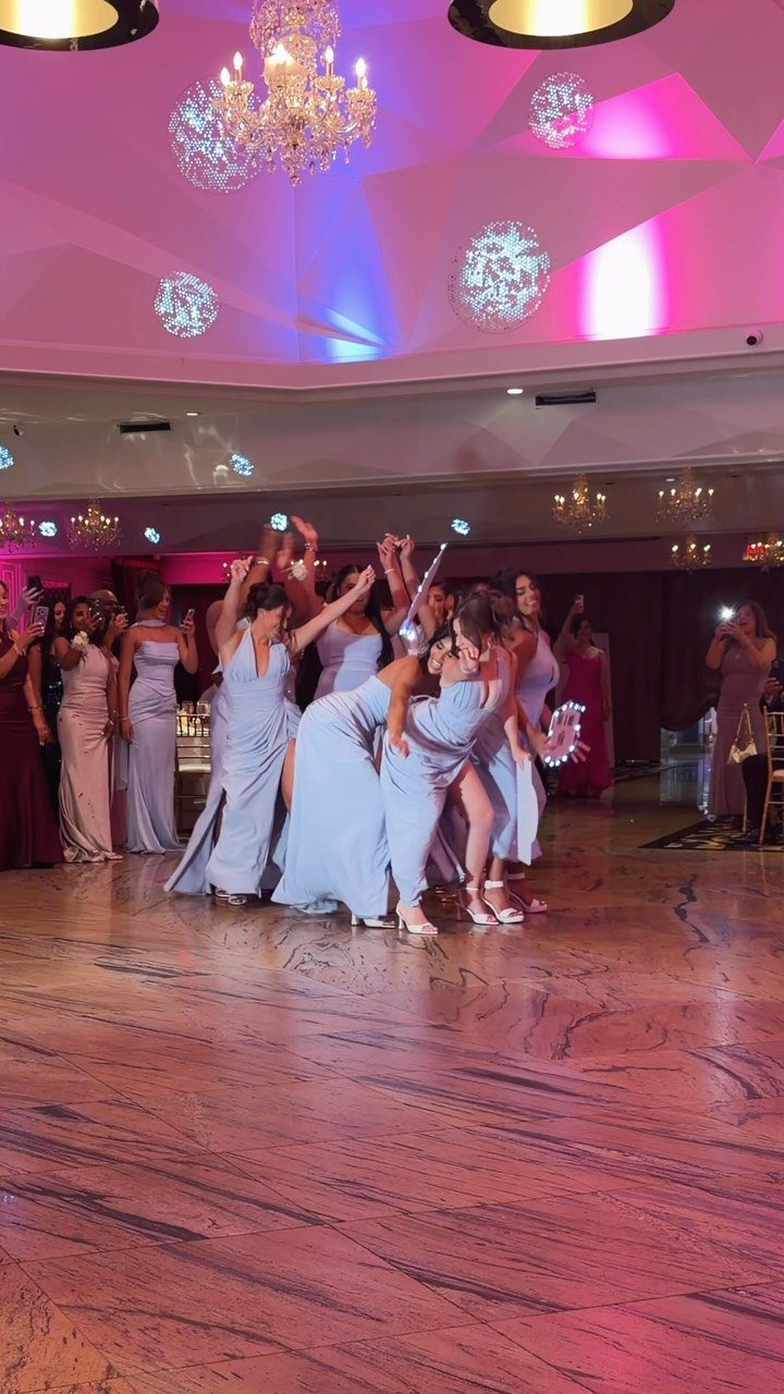 Women in formal gowns performing a choreographed dance in a lit ballroom.