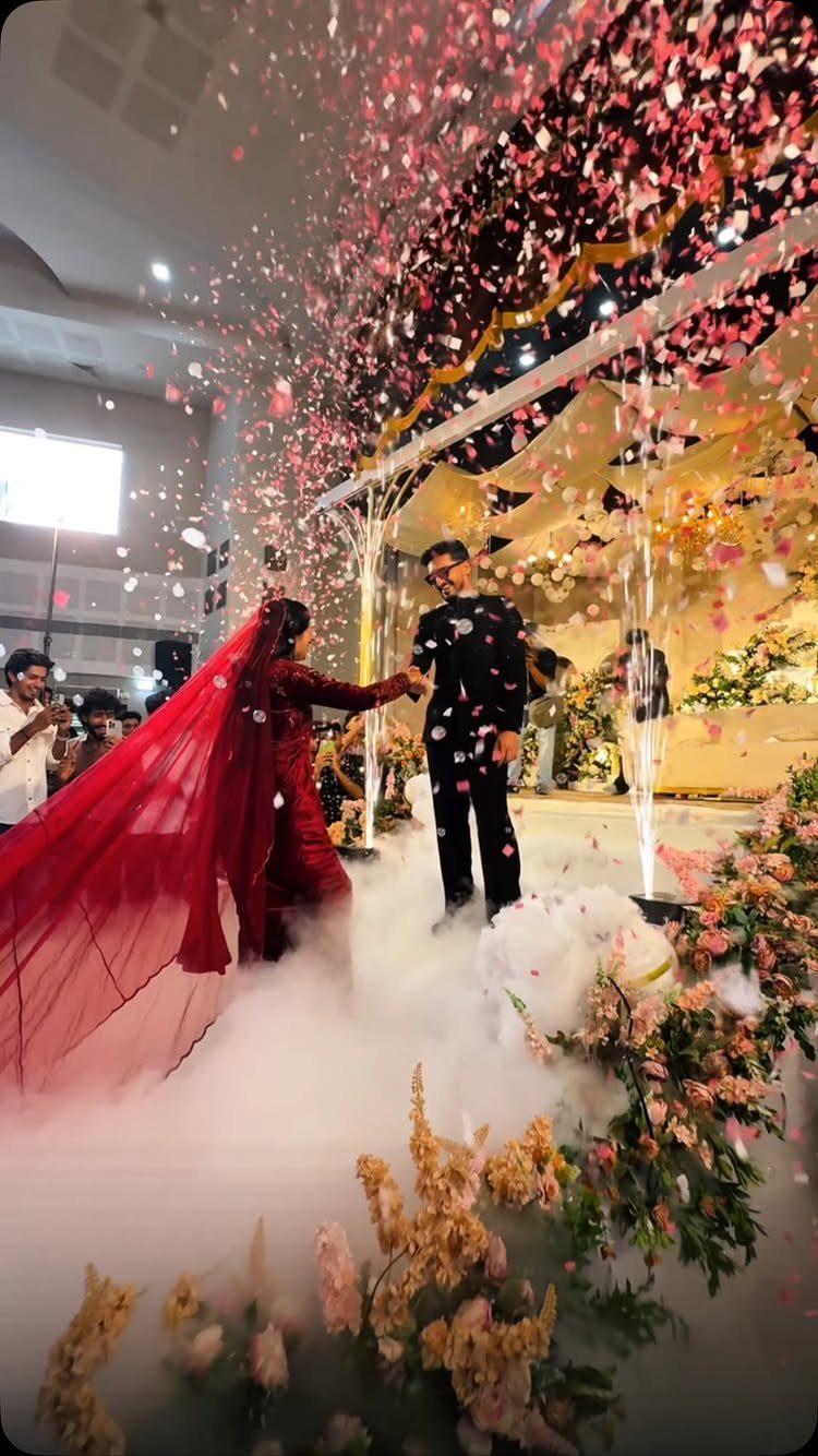 Couple walking through white smoke and falling pink confetti at a wedding entrance.