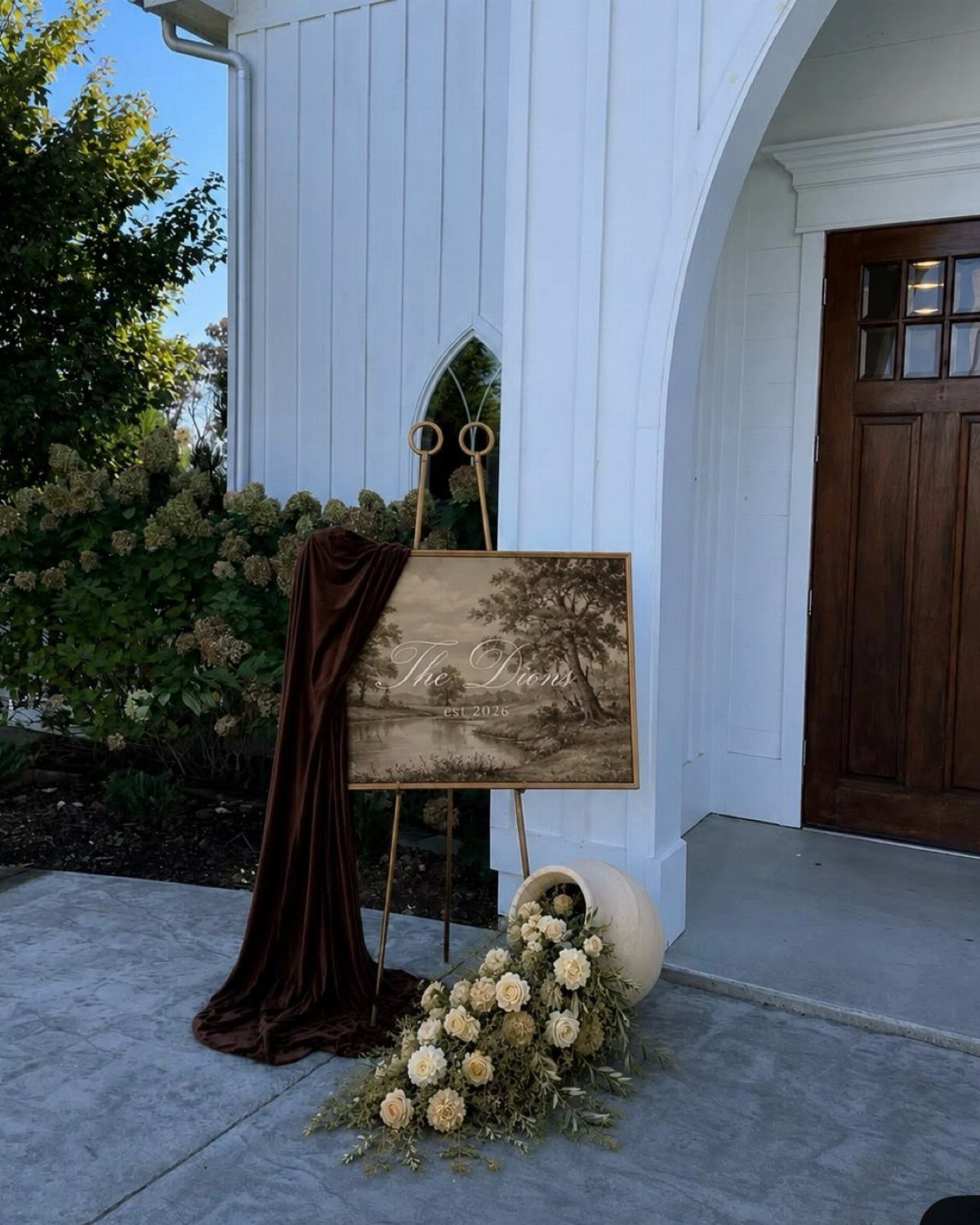 Wooden welcome sign on a gold easel with brown velvet and cream flowers.