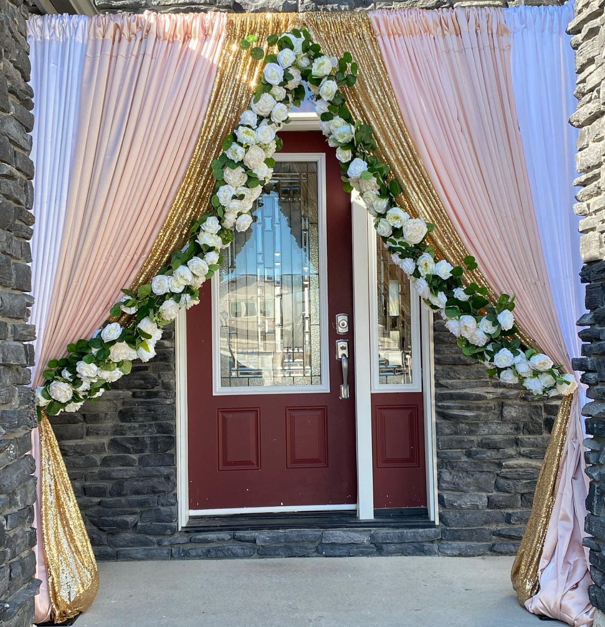 Red front door decorated with pink curtains, gold sequins, and a white rose garland.