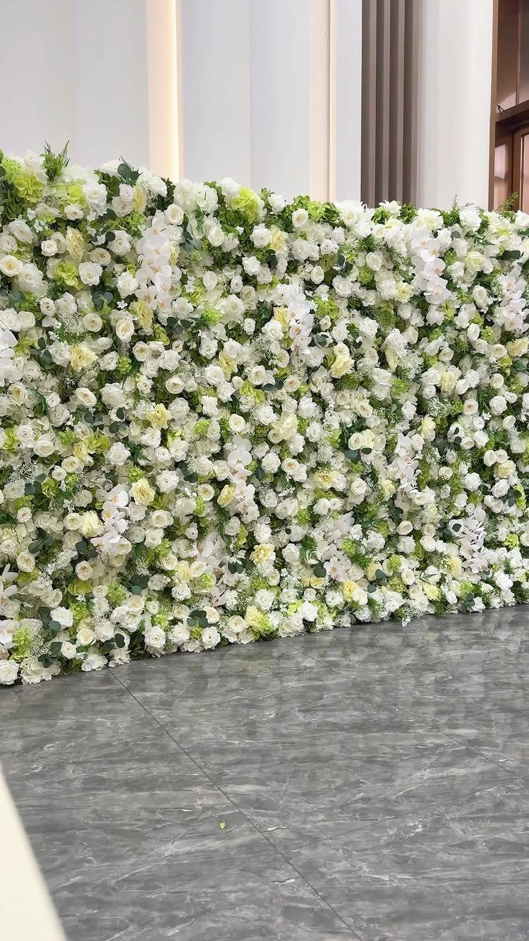 Floral wall made of white and cream flowers with green leaves on grey flooring.