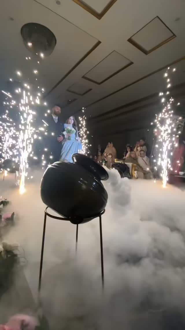 Couple standing amidst thick white smoke and bright sparkler fountains at wedding entrance