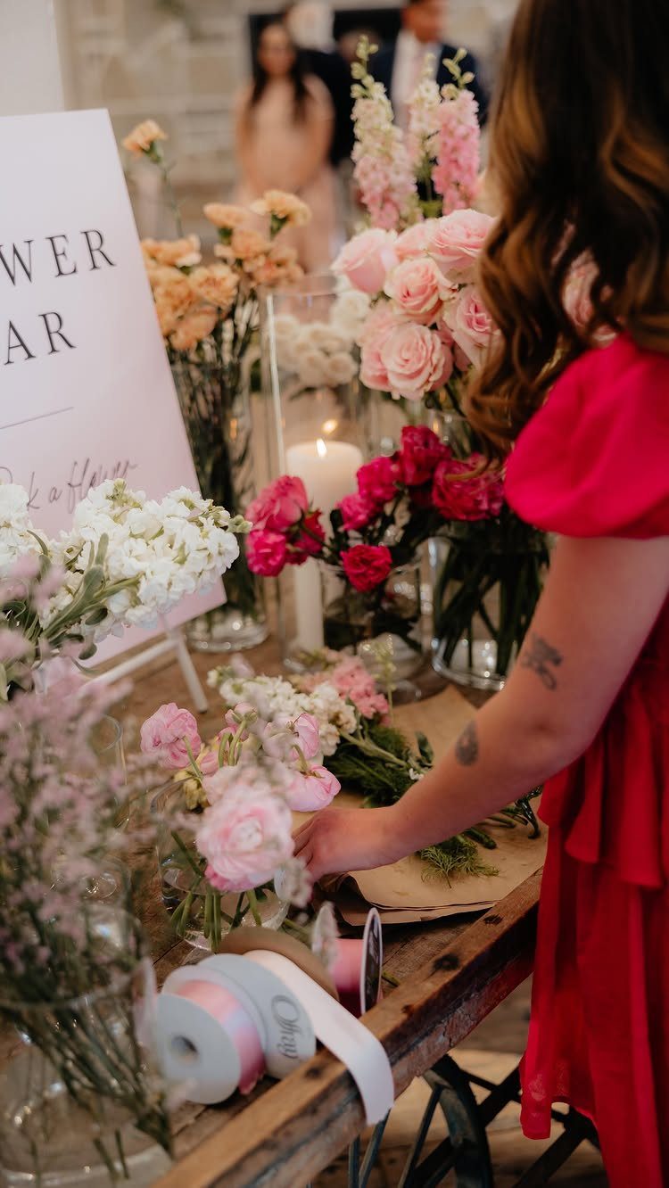 13 Wedding Reception Ideas for Guests Who Love Fun 8 Woman in red dress arranging flowers at a wedding flower bar station.