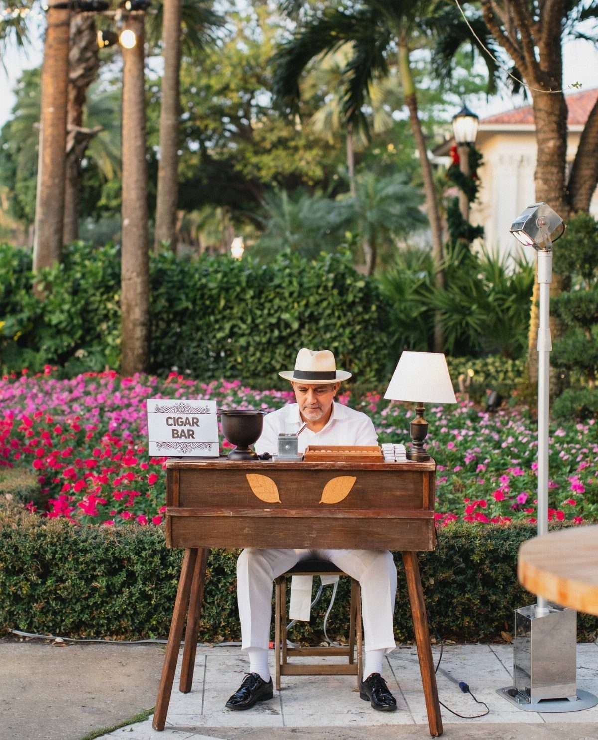 13 Wedding Reception Ideas for Guests Who Love Fun 9 Cigar roller in white clothing and hat working at a wooden outdoor station.