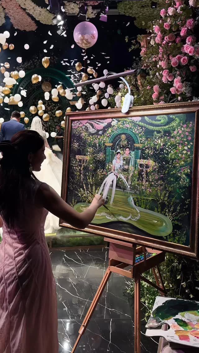 13 Wedding Reception Ideas for Guests Who Love Fun 3 Artist in pink dress painting a wedding couple on a canvas at a reception.