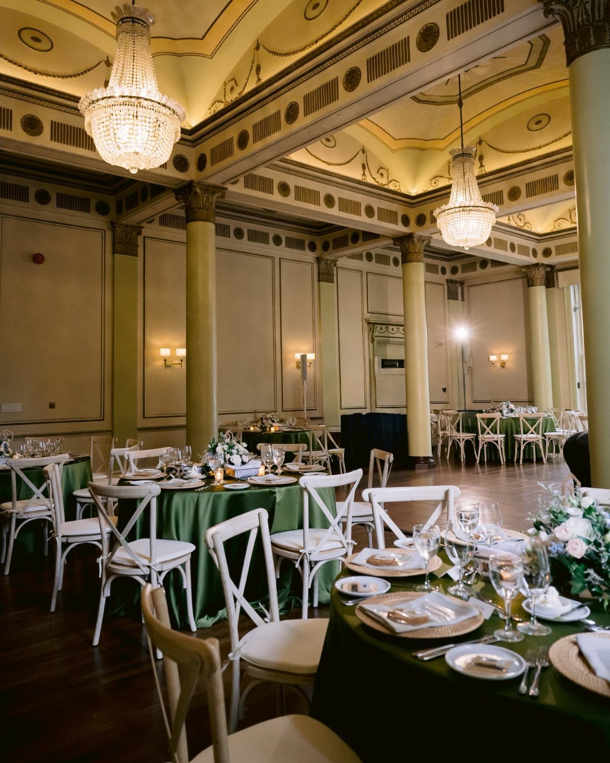 17 Wedding Reception Venues for Every Style and Budget 6 Elegant ballroom with green clothed tables, white chairs, and large crystal chandeliers.