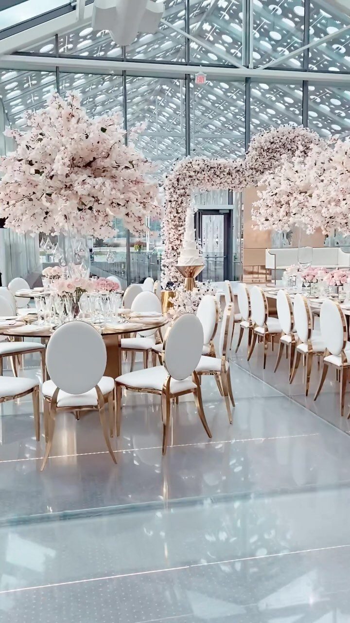 17 Wedding Reception Venues for Every Style and Budget 14 Elegant event space with pink cherry blossom arrangements, white chairs, and reflective flooring.