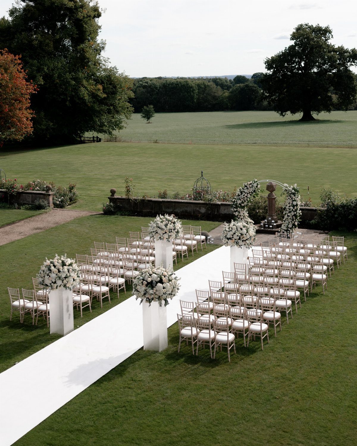 17 Wedding Reception Venues for Every Style and Budget 1 Outdoor wedding ceremony setup with white chairs, floral arrangements, and a white aisle runner.