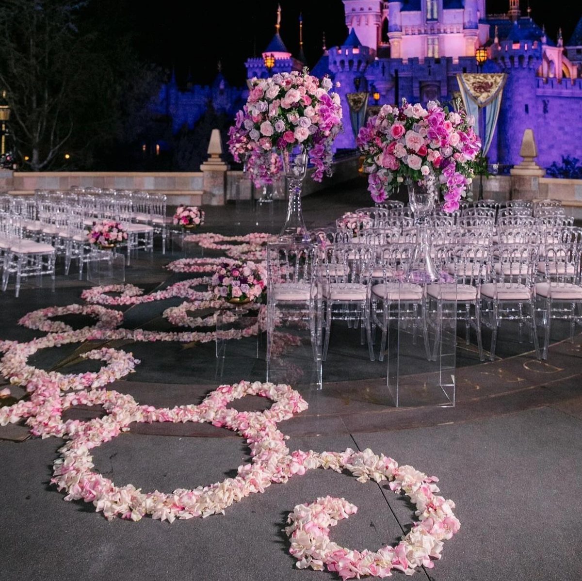 17 Wedding Reception Venues for Every Style and Budget 12 Wedding ceremony setup with pink flowers and acrylic chairs before a lit castle.