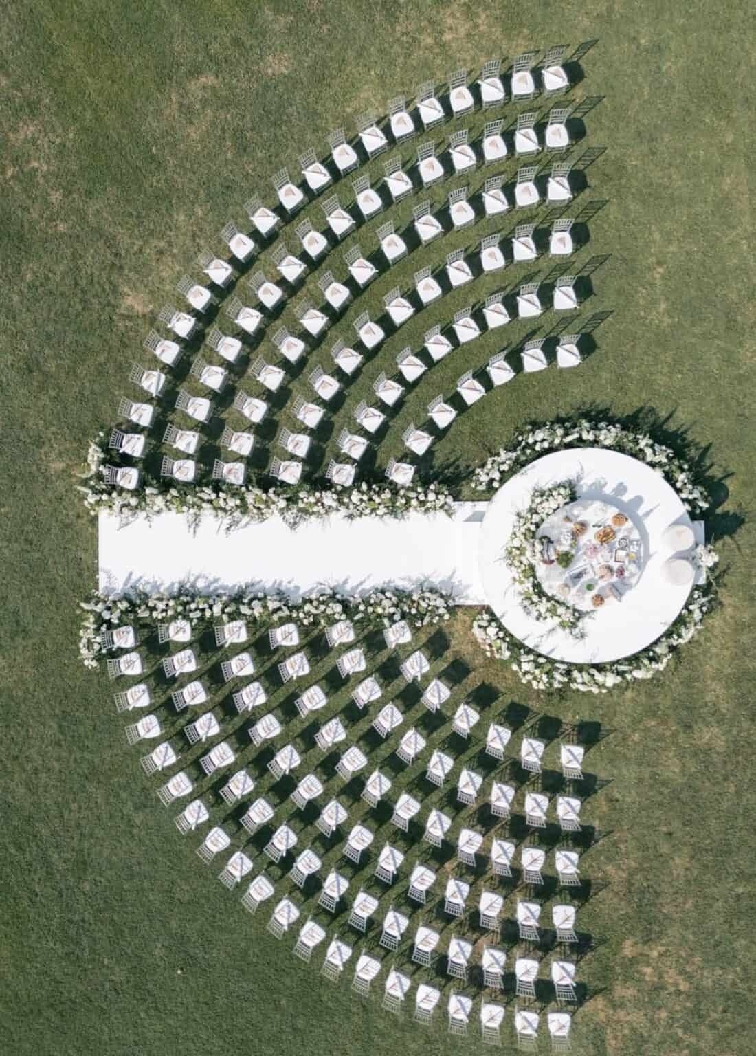 Curved rows of white chairs and a circular altar on a green lawn.