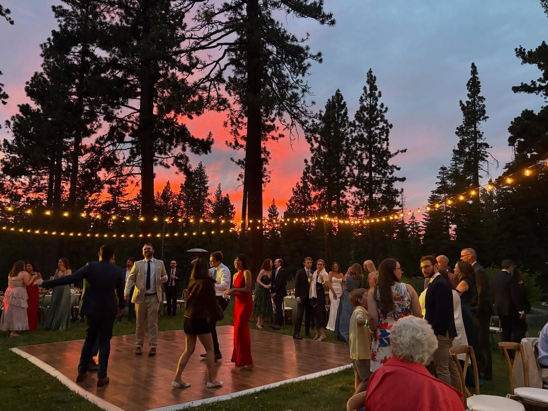 Wooden outdoor dance floor with string lights and guests under a red sunset sky.
