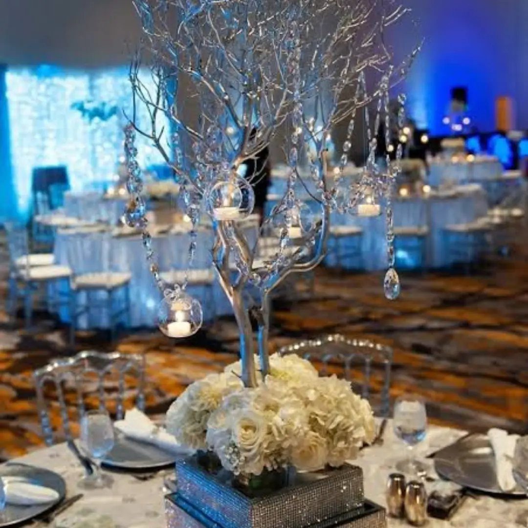 Silver decorative tree with crystals and candles atop white flowers in a ballroom