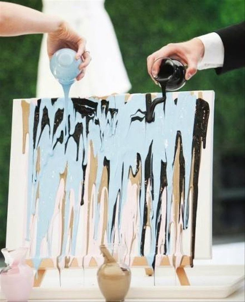 Two people pouring blue and black paint onto a canvas for a unity painting.