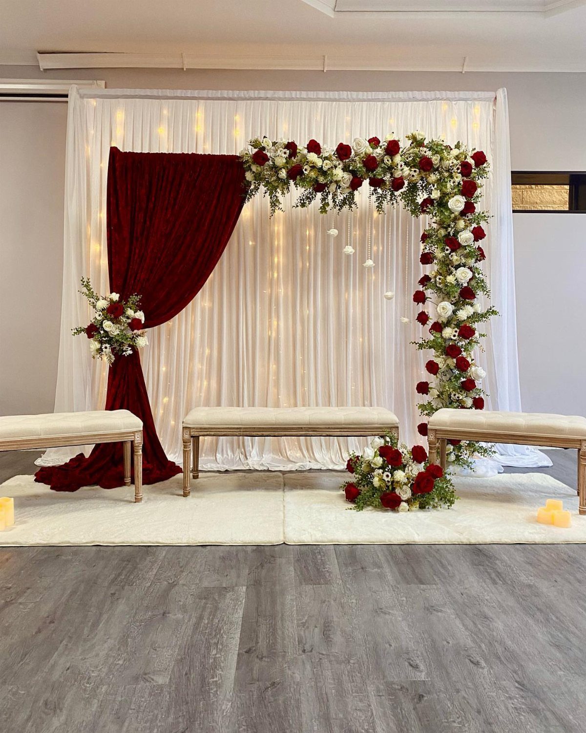 7 Wedding Stage Decorations for Romantic Receptions 2 Wedding stage with cascading red and white roses, red velvet drapery, and white curtains.