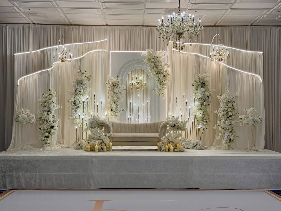 7 Wedding Stage Decorations for Romantic Receptions 4 Wedding stage with white drapery, floral arrangements, and crystal chandeliers over a sofa.