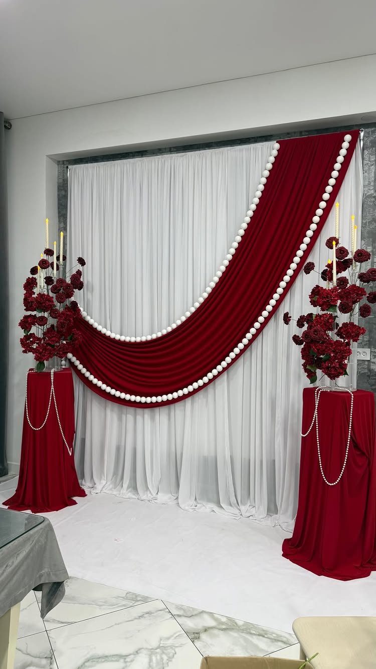 7 Wedding Stage Decorations for Romantic Receptions 1 Red velvet drapery with pearls over a white backdrop with red rose arrangements.